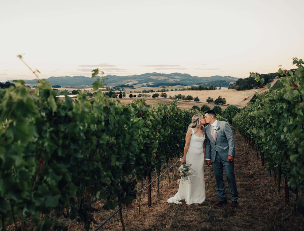 Oregon bride and groom kiss in a vineyard during sunset at Left Coast Cellars in Rickreal oregon