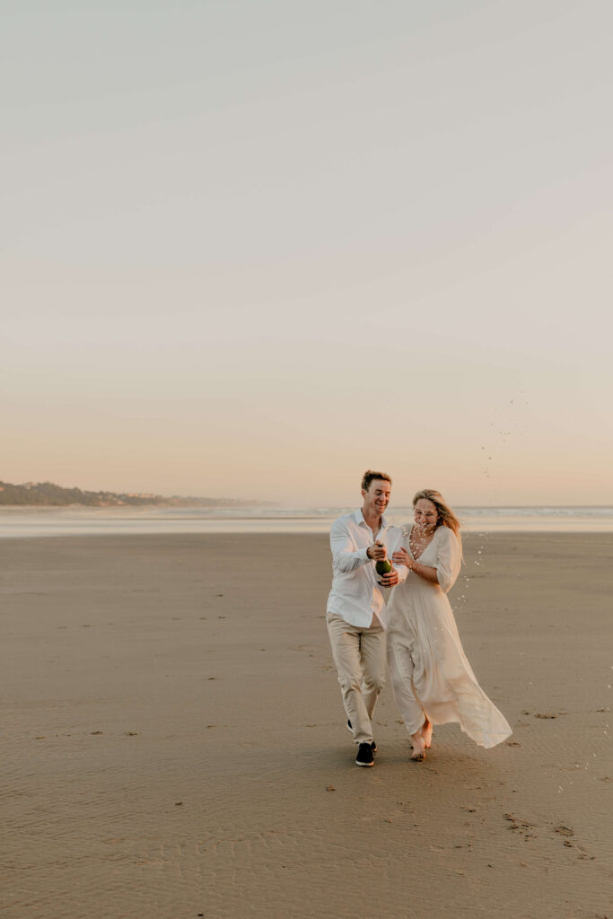 Couple pops a bottle of bubbly at a beach engagement session