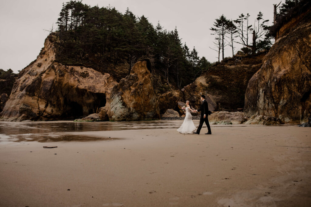 Couple walking across the sand at a Hug Point elopement in Oregon.