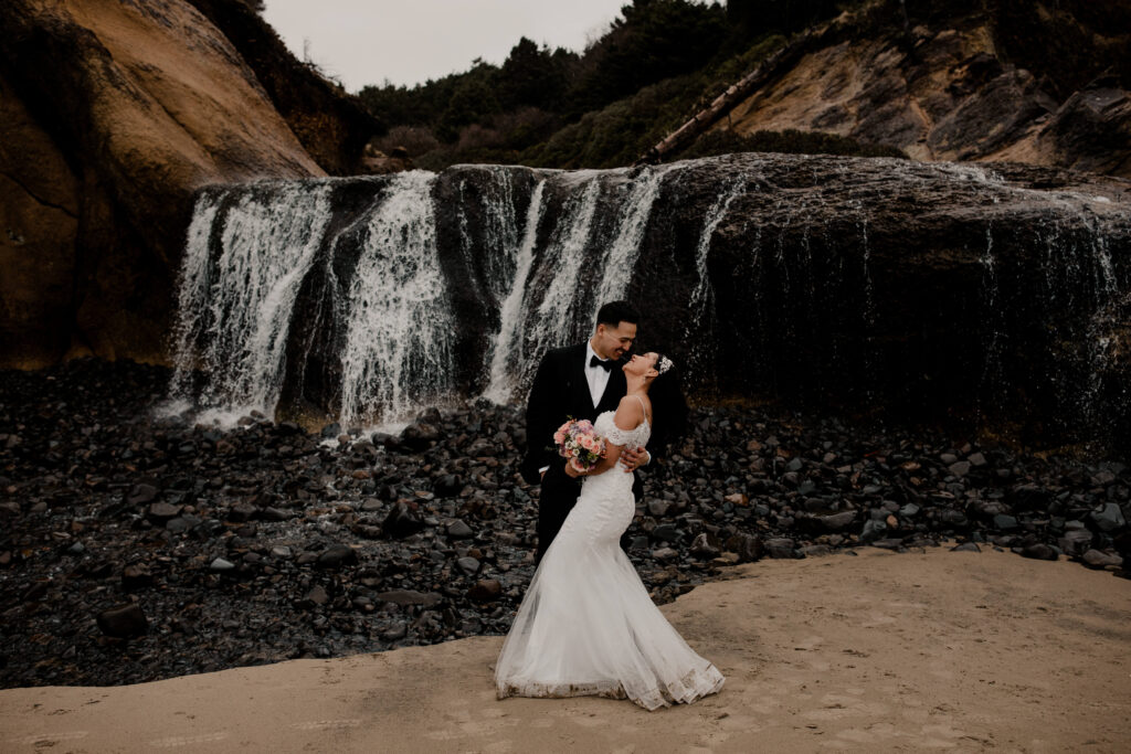 Couple walks through the water under a waterfall at hug point