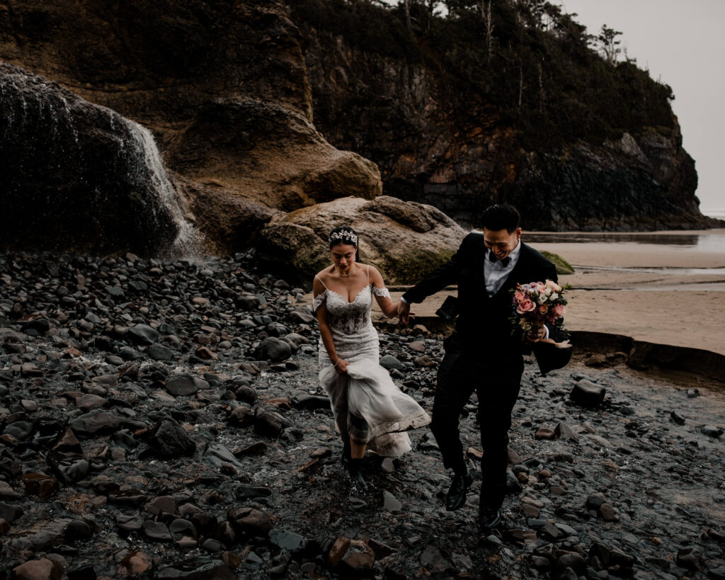 Couple walks through the water under a waterfall at hug point