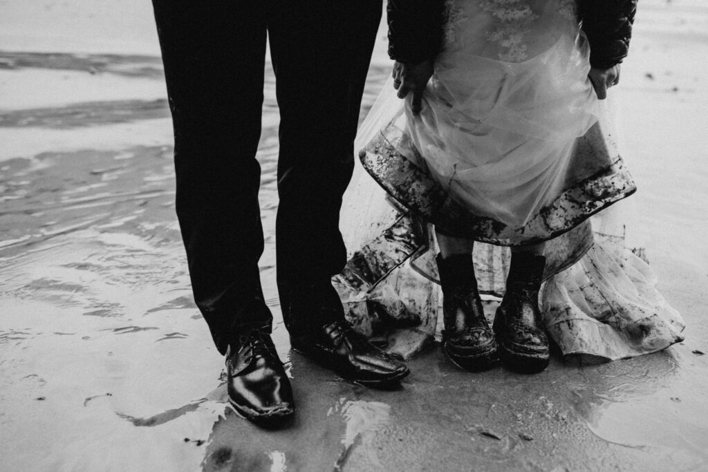 A close up of a bride and grooms boots on the sand at a hug point elopement