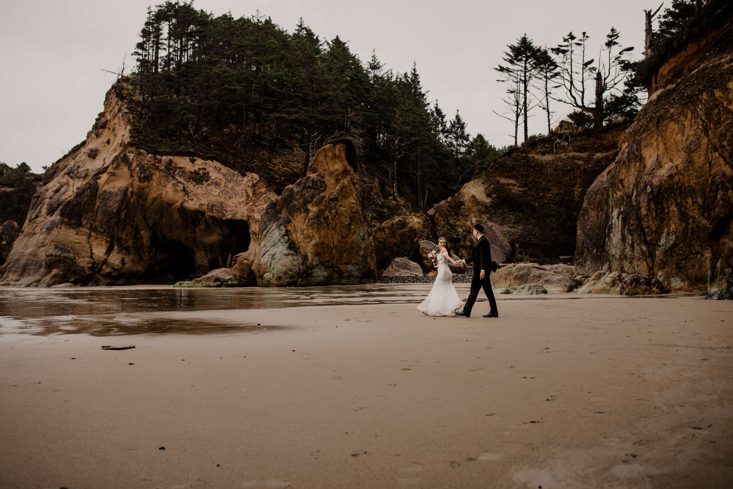 Couple walking across the sand at a Hug Point elopement in Oregon.