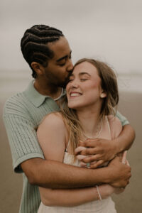 Couple snuggles on the beach at an Oregon coast engagement session shot by Ronny and Rene.