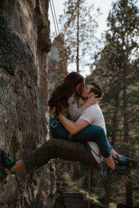 couple hiking together kissing on smith rock cliffside engagement photoshoot