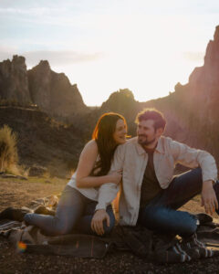 fiancee hugs fiancé's arm as they lay on blanket at smith rock engagement photoshoot