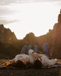 engaged couple lays on the ground at smith rock holding hands and looking at each other