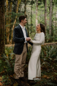 wedding couple hold hands and laugh in olympic national park forest