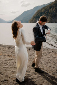 wedding couple popping champagne and laughing in front of lake at olympic national park