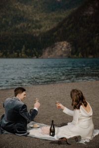 elopement couple at olympic national park lake drinking champagne and eating cake