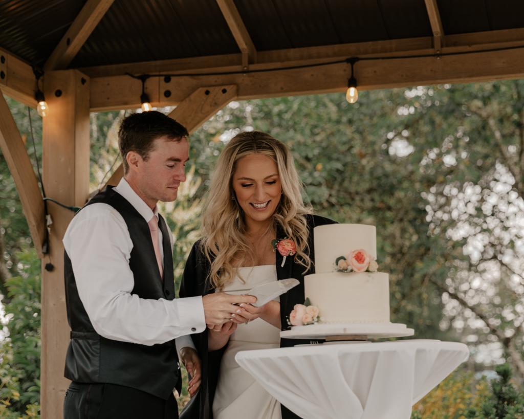 wedding couple cutting wedding cake under outdoor gazebo at corvallis club in oregon