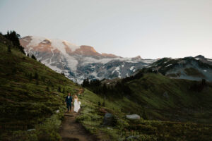 couple walks hand in hand while hiking mount rainier with landscape behind after eloping