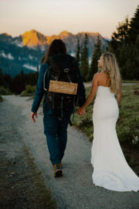 couple holds hands while hiking after elopement with just married sign on backpack gear