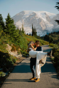 groom holds bride in arms as they kiss with Mount Rainier landscape behind them