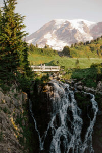 elopement couple stand far away on a bridge above a waterfall in mount rainier landscape for their elopement