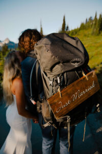 couple hikes away from their elopement ceremony with a just married sign on their backpack gear