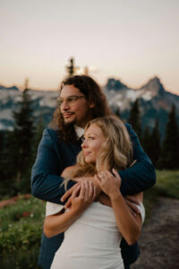 groom holds bride in arms as they look in distance at mount rainier