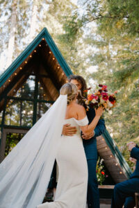 elopement couple kisses in mount rainier cabin with bright flower bouquet