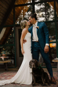 couple poses with their dog and kissing in front of mount rainier cabin for elopement
