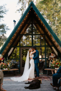 bride and groom kiss at elopement ceremony at mount rainier cabin while dog lays in aisle