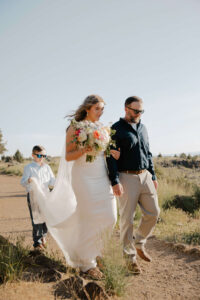 Bride walking down the aisle with her father and brother holding her train at Smith Rock Elopement