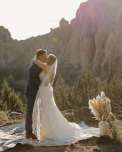 Bride and groom kiss against the dramatic cliffs of Smith Rock.