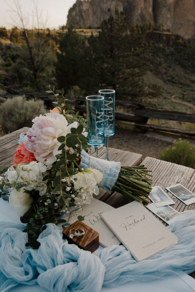 Bridal bouquet with pastel blooms arranged next to vow books and rings at Smith Rock State Park