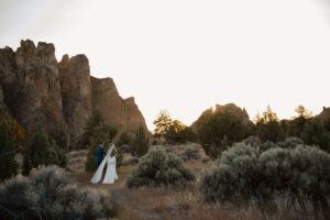 Bride and groom walking together through grassy terrain at Smith Rock State Park.