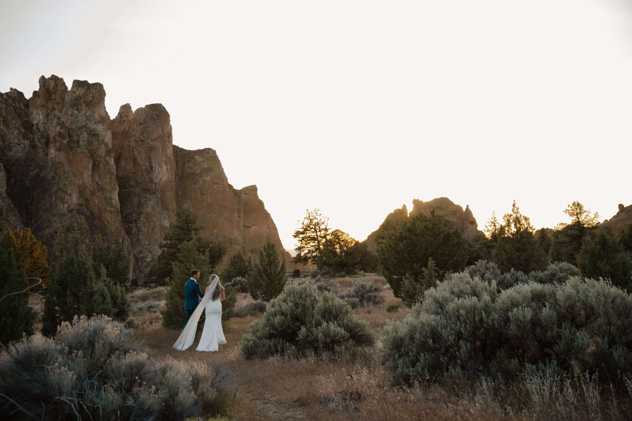 Bride and groom walking together through grassy terrain at Smith Rock State Park.