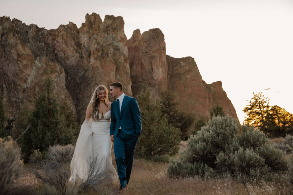 Bride and groom walking together through grassy terrain at Smith Rock State Park.