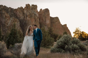 Bride and groom walking together through grassy terrain at Smith Rock State Park.