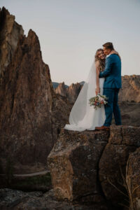 Couple embracing on an overlook with Smith Rock formations in the background.