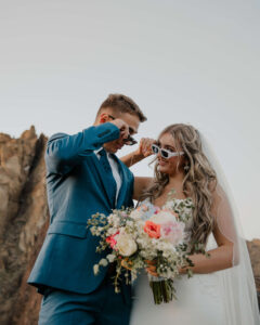 Bride wearing sunglasses and holding bouquet while standing with groom at Smith Rock.