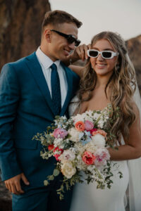 Bride wearing sunglasses and holding bouquet while standing with groom at Smith Rock.