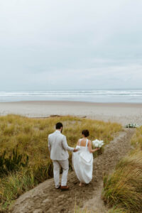 Groom holds his brides train as she walks down a sand aisle for their vow renewal