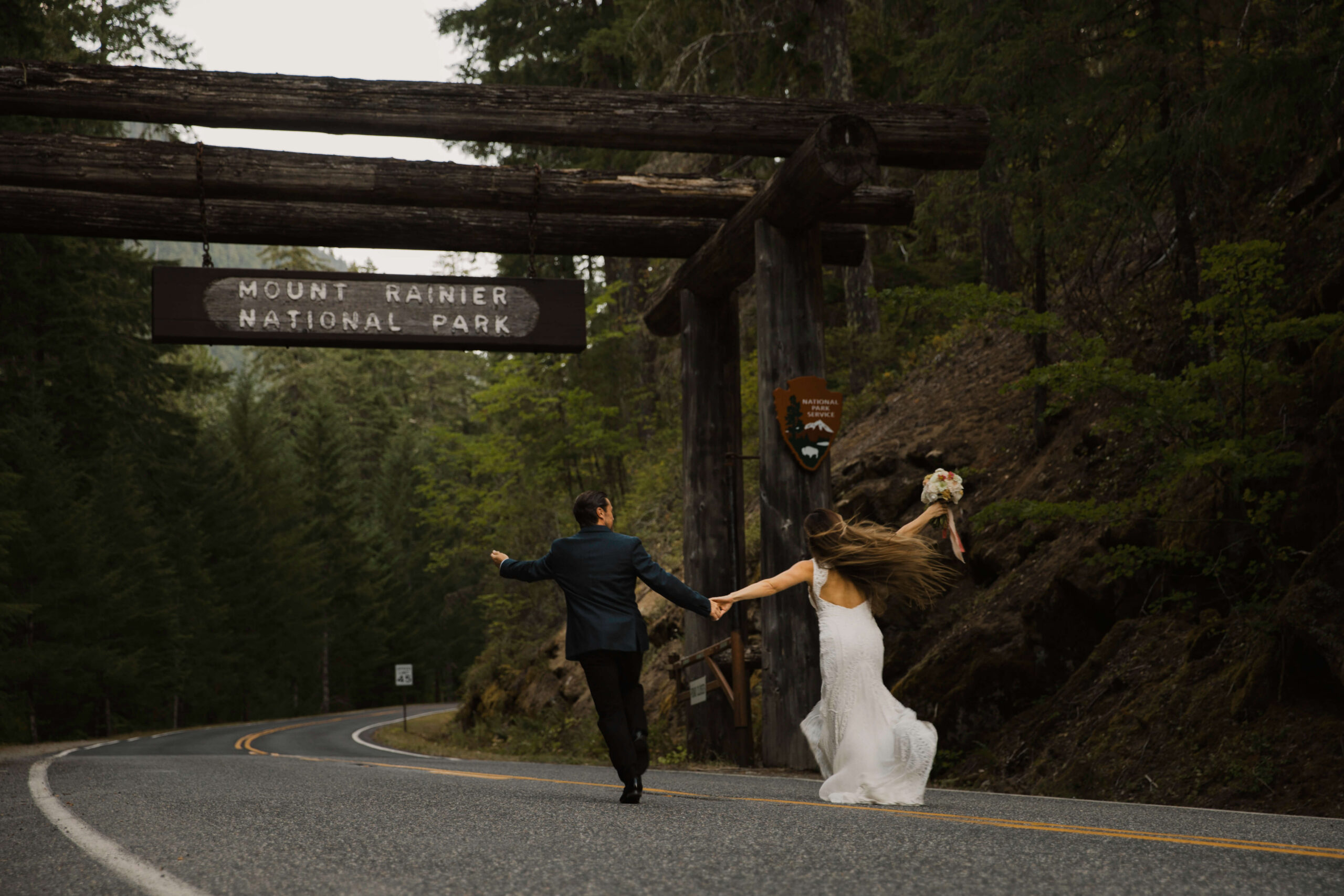 couple runs together under the mount rainier national park sign